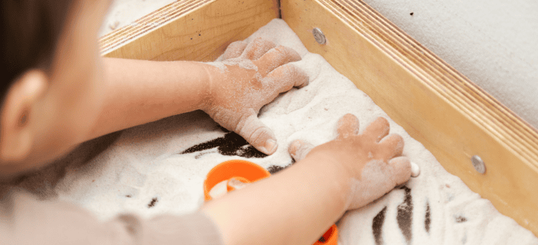 FCSS Case Study. Picture of a little girl enjoying sensory plan with her hands in sand.